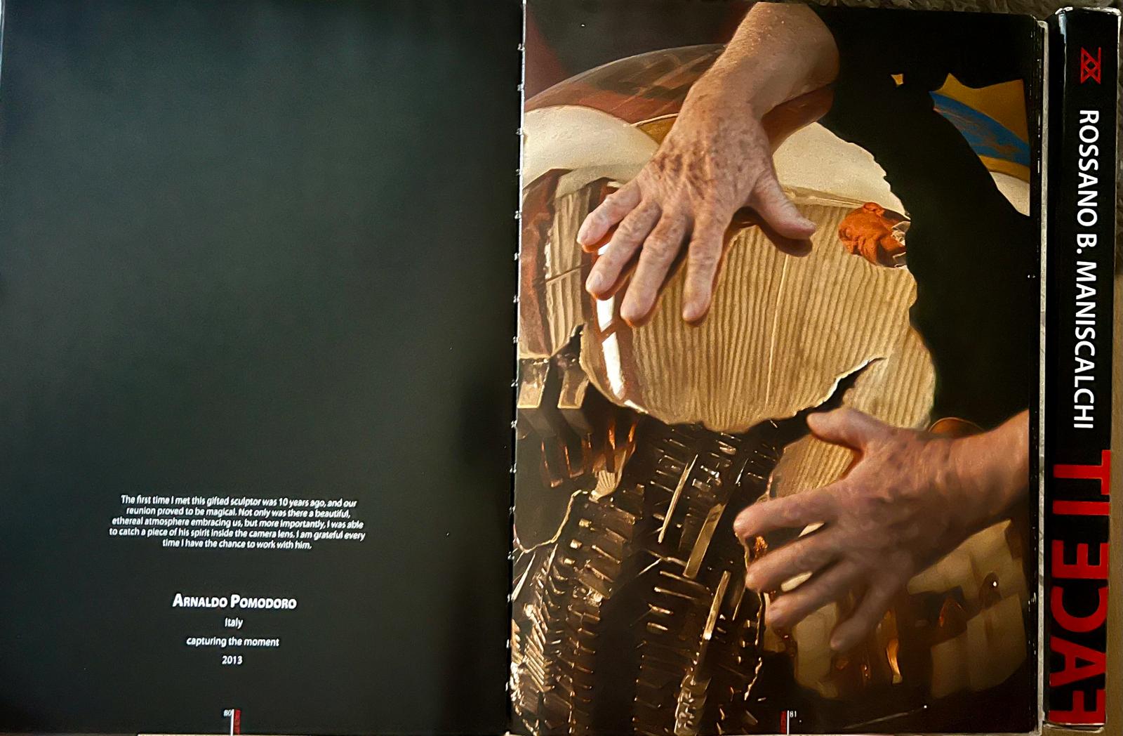 Le mani di Arnaldo Pomodoro appoggiate su una sua sfera dorata, fotografate da Rossano B. Maniscalchi; accanto, la pagina con la dedica dell'artista.